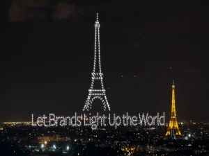 Crostars drones forming Eiffel Tower and Let Brands Light Up the World text beside real Eiffel Tower, Paris