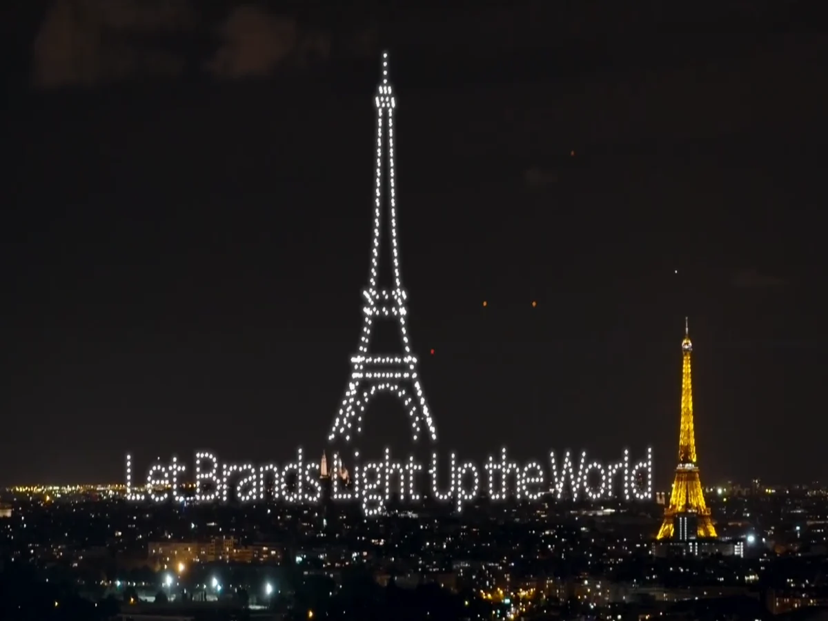 Crostars drones forming Eiffel Tower and Let Brands Light Up the World text beside real Eiffel Tower, Paris