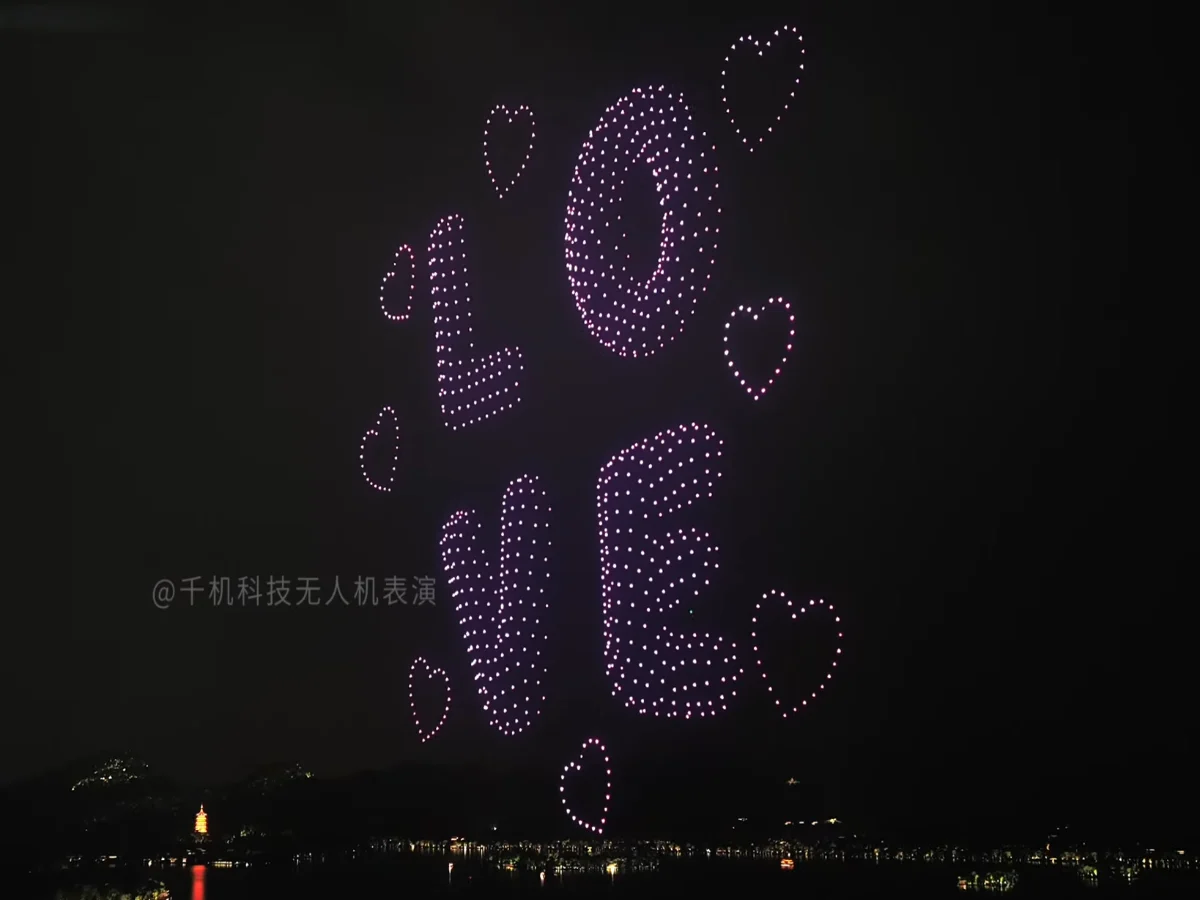 Drones forming the word LOVE with glowing hearts over a lake at night, a romantic drone show formation